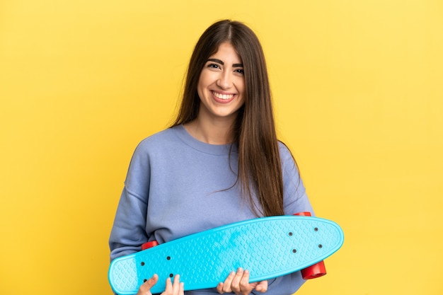 Jeune femme caucasienne isolée sur fond jaune avec un patin avec une expression heureuse