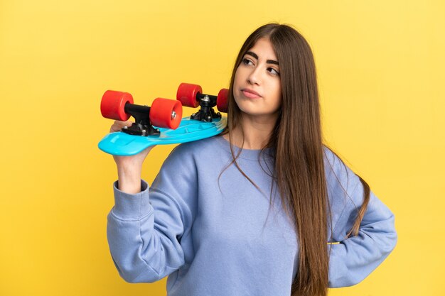 Jeune femme caucasienne isolée sur fond jaune avec un patin