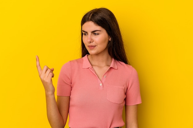 Jeune femme caucasienne isolée sur fond jaune pointant avec le doigt sur vous comme si vous invitiez à vous rapprocher.