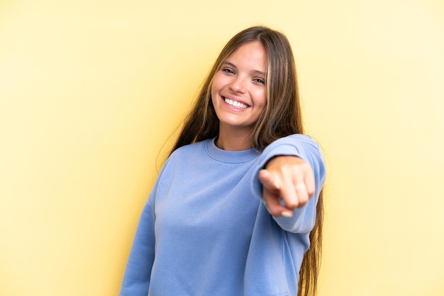 Jeune femme caucasienne isolée sur fond jaune pointant vers l'avant avec une expression heureuse