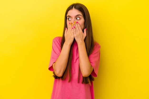 Jeune femme caucasienne isolée sur fond jaune réfléchie à la recherche d'un espace de copie couvrant la bouche avec la main.