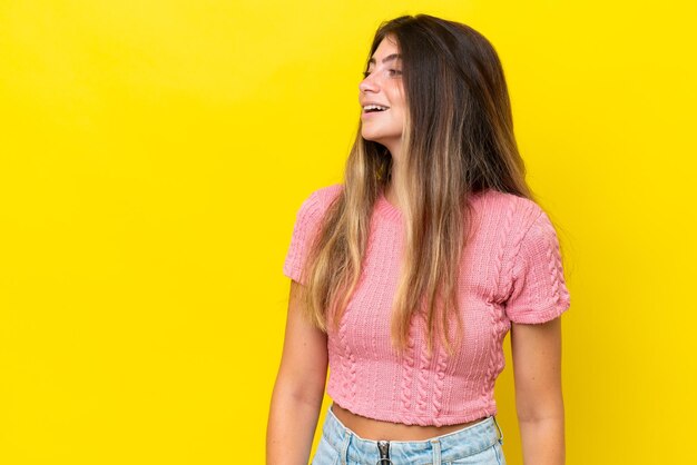 Jeune femme caucasienne isolée sur fond jaune riant en position latérale