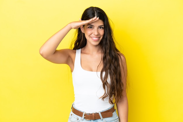 Jeune femme caucasienne isolée sur fond jaune saluant avec la main avec une expression heureuse