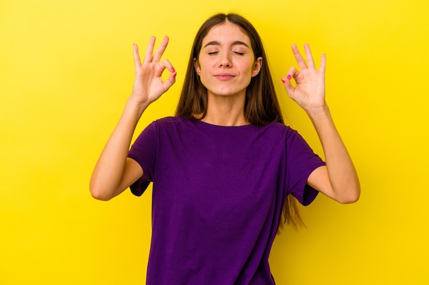 Jeune femme caucasienne isolée sur fond jaune se détend après une dure journée de travail, elle fait du yoga.