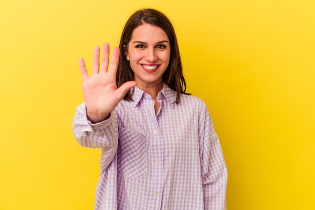 Jeune femme caucasienne isolée sur fond jaune souriant joyeux montrant le numéro cinq avec les doigts