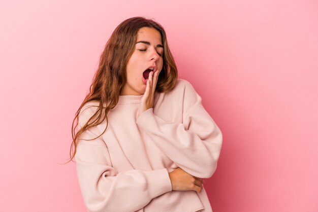 Jeune femme caucasienne isolée sur fond rose bâillant montrant un geste fatigué couvrant la bouche avec la main.