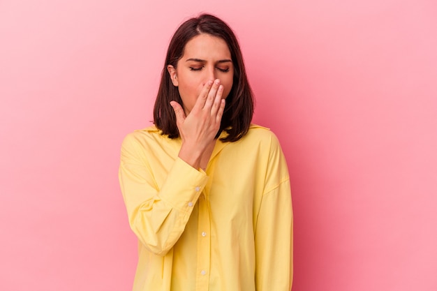 Jeune femme caucasienne isolée sur fond rose bâillant montrant un geste fatigué couvrant la bouche avec la main.