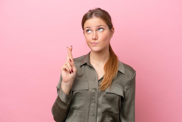 Jeune femme caucasienne isolée sur fond rose avec les doigts croisés et souhaitant le meilleur