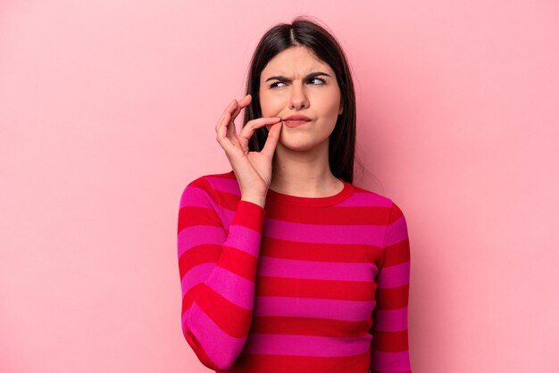 Jeune femme caucasienne isolée sur fond rose avec les doigts sur les lèvres en gardant un secret