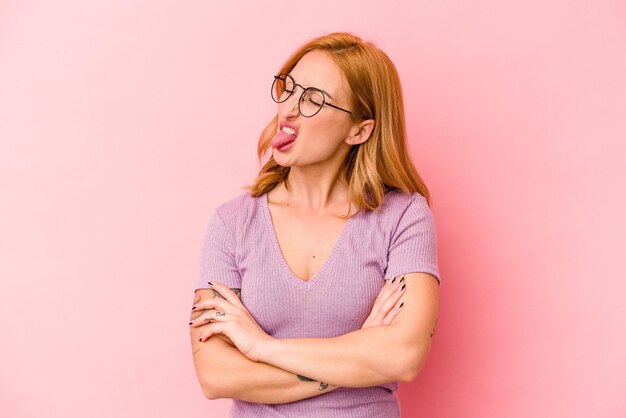 Jeune femme caucasienne isolée sur fond rose drôle et sympathique qui sort la langue.