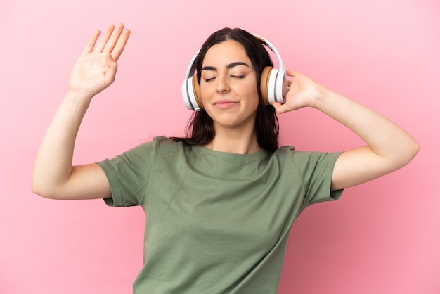 Jeune femme caucasienne isolée sur fond rose, écouter de la musique et danser