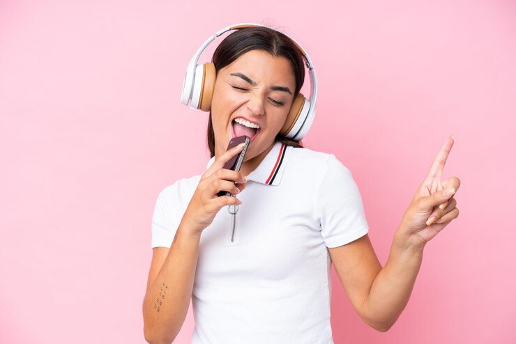 Photo jeune femme caucasienne isolée sur fond rose, écouter de la musique avec un mobile et chanter