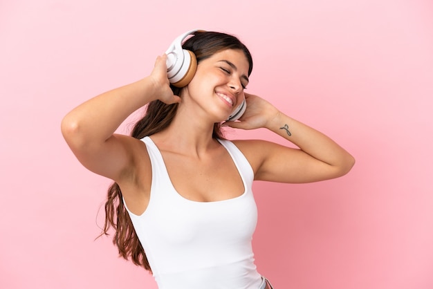 Jeune femme caucasienne isolée sur fond rose, écouter de la musique