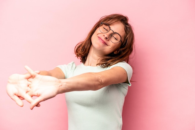 Jeune femme caucasienne isolée sur fond rose étirant les bras en position détendue