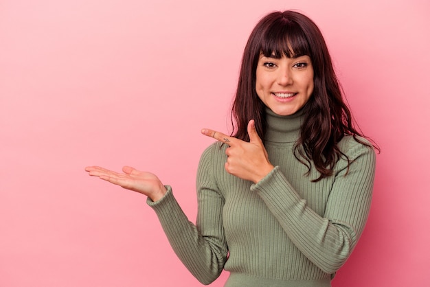 Jeune femme caucasienne isolée sur fond rose excité tenant un espace de copie sur la paume.