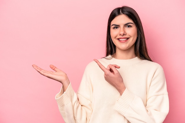 Jeune femme caucasienne isolée sur fond rose excitée tenant un espace de copie sur la paume