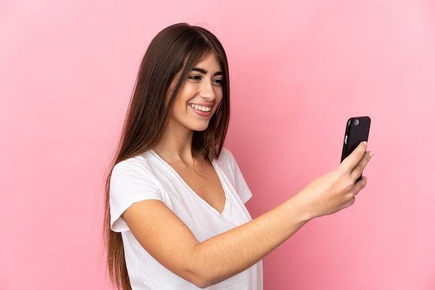 Jeune femme caucasienne isolée sur fond rose faisant un selfie avec un téléphone portable