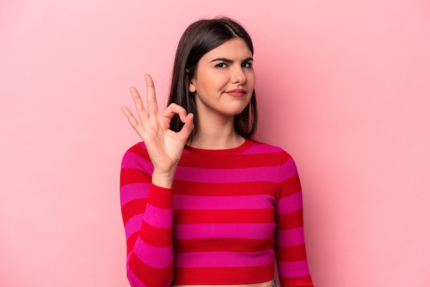 Jeune femme caucasienne isolée sur fond rose fait un clin d'œil et tient un geste correct avec la main