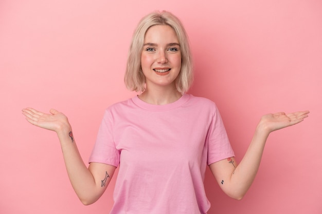 Jeune femme caucasienne isolée sur fond rose fait l'échelle avec les bras, se sent heureuse et confiante.