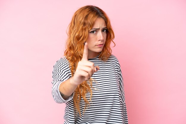 Une jeune femme caucasienne isolée sur un fond rose frustrée et pointant vers l'avant