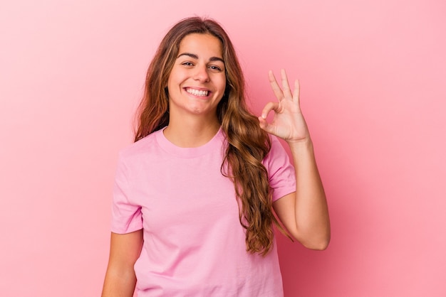 Jeune femme caucasienne isolée sur fond rose gaie et confiante montrant un geste ok.