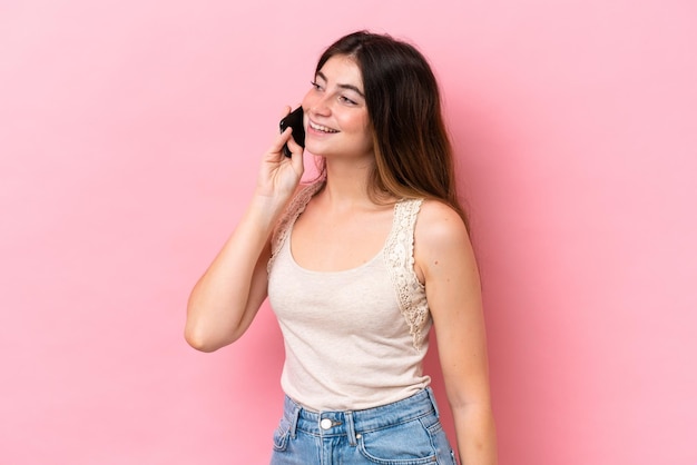 Jeune femme caucasienne isolée sur fond rose gardant une conversation avec le téléphone portable