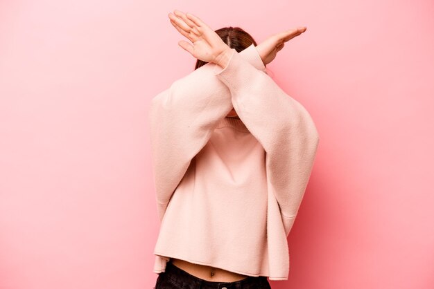 Jeune femme caucasienne isolée sur fond rose en gardant les deux bras croisés concept de déni