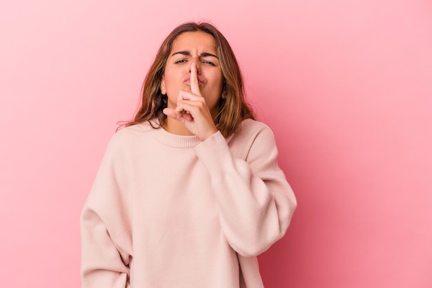 Jeune femme caucasienne isolée sur fond rose gardant un secret ou demandant le silence.