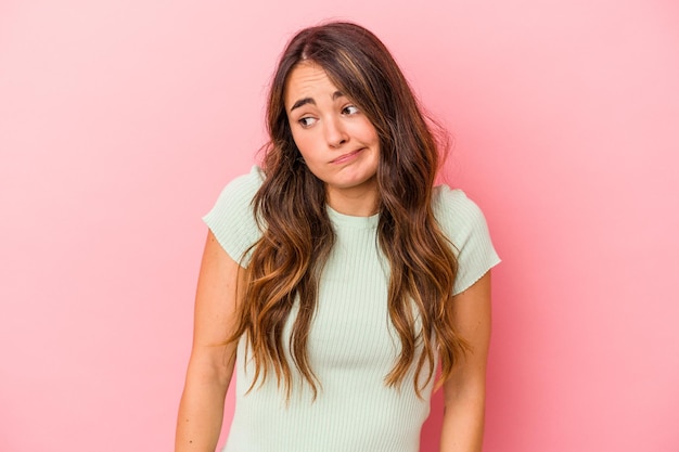 Jeune femme caucasienne isolée sur fond rose hausse les épaules et ouvre les yeux confus.