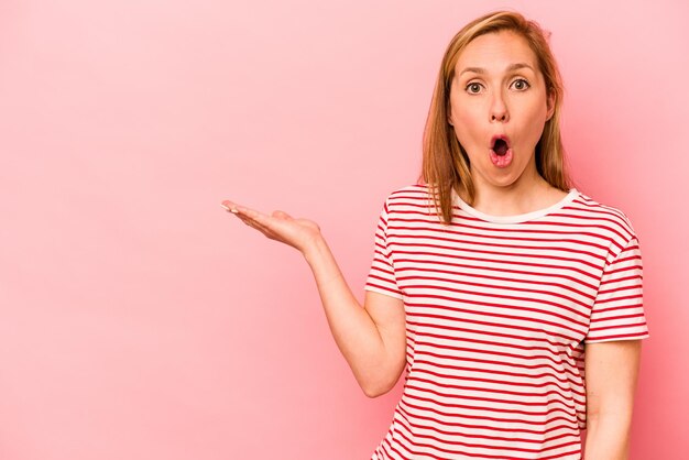 Jeune femme caucasienne isolée sur fond rose impressionné tenant l'espace de copie sur la paume