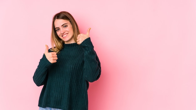 Jeune femme caucasienne isolée sur fond rose, levant les deux pouces vers le haut, souriant et confiant.