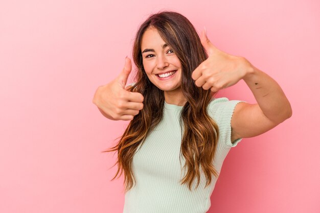 Jeune femme caucasienne isolée sur fond rose levant les deux pouces vers le haut, souriante et confiante.