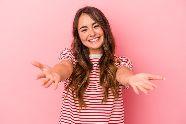 Jeune femme caucasienne isolée sur fond rose montrant une expression bienvenue.