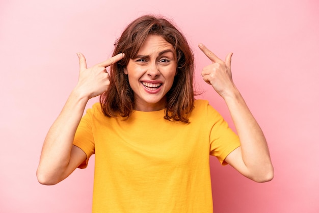 Jeune femme caucasienne isolée sur fond rose montrant un geste de déception avec l'index