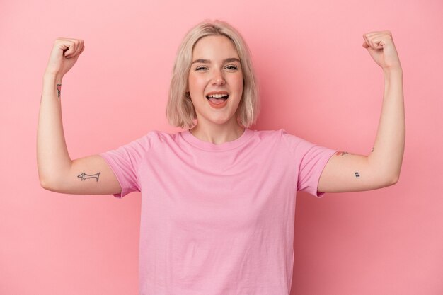 Jeune femme caucasienne isolée sur fond rose montrant un geste de force avec les bras, symbole du pouvoir féminin