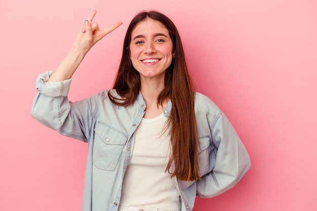 Jeune femme caucasienne isolée sur fond rose montrant un geste rock avec les doigts