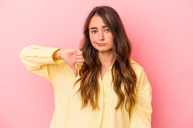 Jeune femme caucasienne isolée sur fond rose montrant le pouce vers le bas, concept de déception.