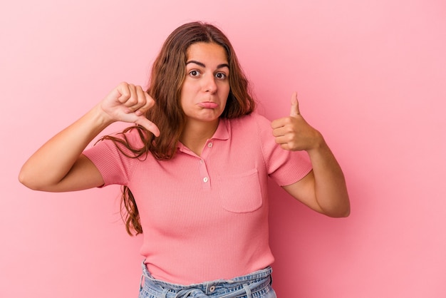 Jeune Femme Caucasienne Isolée Sur Fond Rose Montrant Les Pouces Vers Le Haut Et Les Pouces Vers Le Bas, Concept Difficile à Choisir