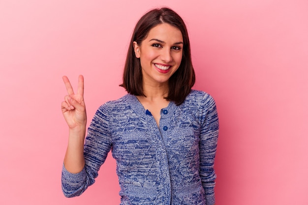 Jeune femme caucasienne isolée sur fond rose montrant le signe de la victoire et souriant largement.