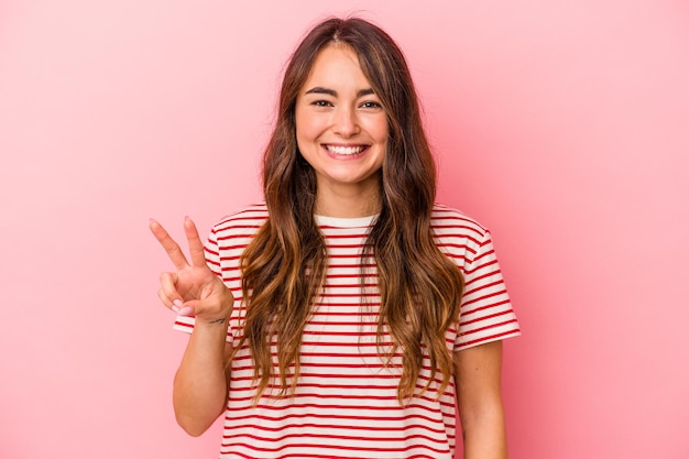 Jeune femme caucasienne isolée sur fond rose montrant le signe de la victoire et souriant largement.