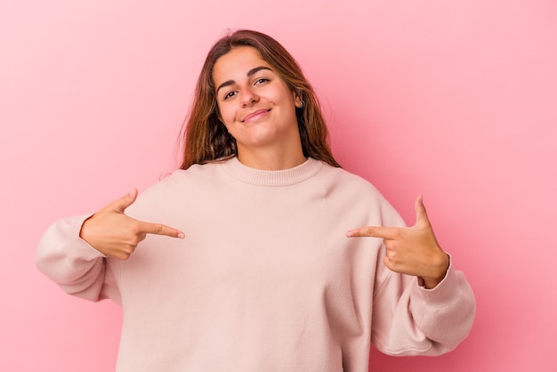 Jeune femme caucasienne isolée sur fond rose personne pointant à la main vers un espace de copie de chemise, fière et confiante