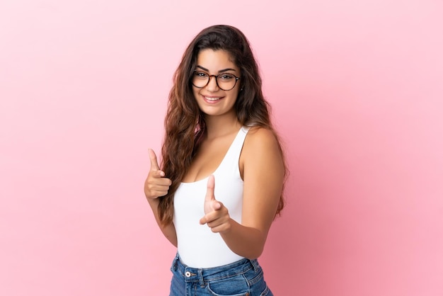 Jeune femme caucasienne isolée sur fond rose pointant vers l'avant et souriant