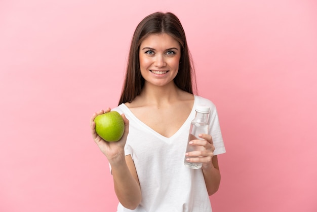 Jeune femme caucasienne isolée sur fond rose avec une pomme et avec une bouteille d'eau