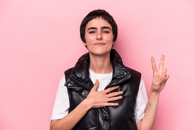 Jeune femme caucasienne isolée sur fond rose prêtant serment, mettant la main sur la poitrine.