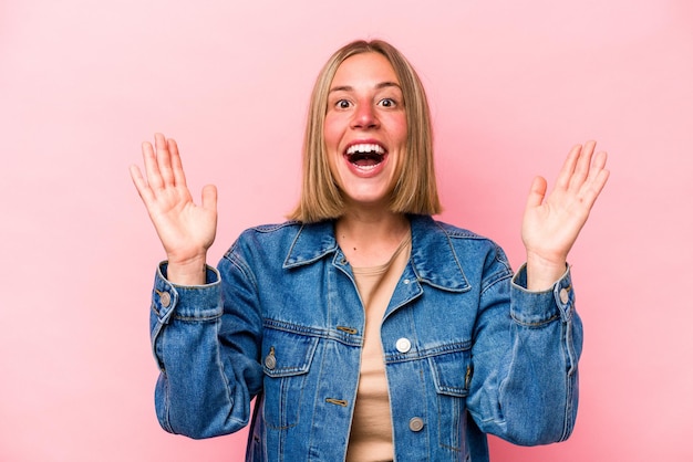 Jeune femme caucasienne isolée sur fond rose recevant une agréable surprise excitée et levant les mains