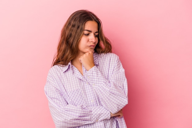 Jeune femme caucasienne isolée sur fond rose regardant de côté avec une expression douteuse et sceptique.