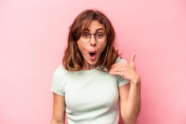 Jeune femme caucasienne isolée sur fond rose riant de quelque chose couvrant la bouche avec les mains