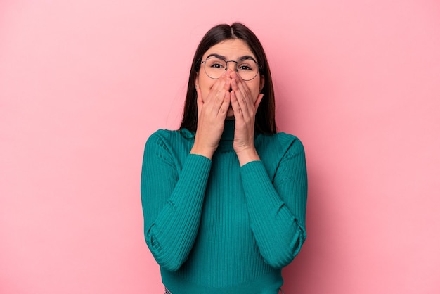 Jeune femme caucasienne isolée sur fond rose riant de quelque chose couvrant la bouche avec les mains