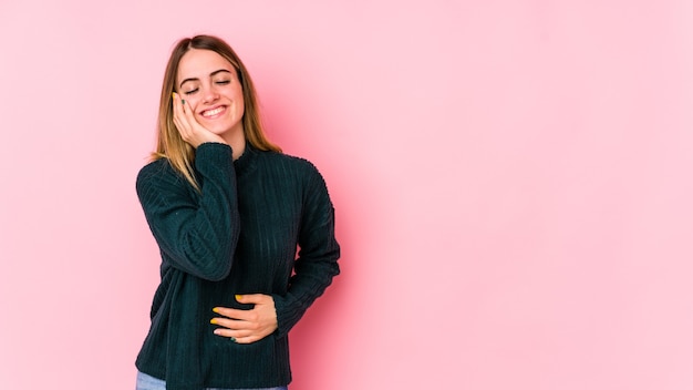 Jeune femme caucasienne isolée sur fond rose rit joyeusement et s'amuse à garder les mains sur le ventre.