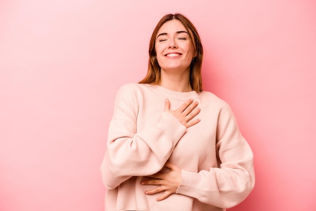 Jeune femme caucasienne isolée sur fond rose rit joyeusement et s'amuse à garder les mains sur le ventre